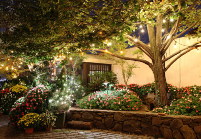 Giardino fiorito illuminato da luci decorative serali, con alberi, aiuole colorate e atmosfera accogliente.